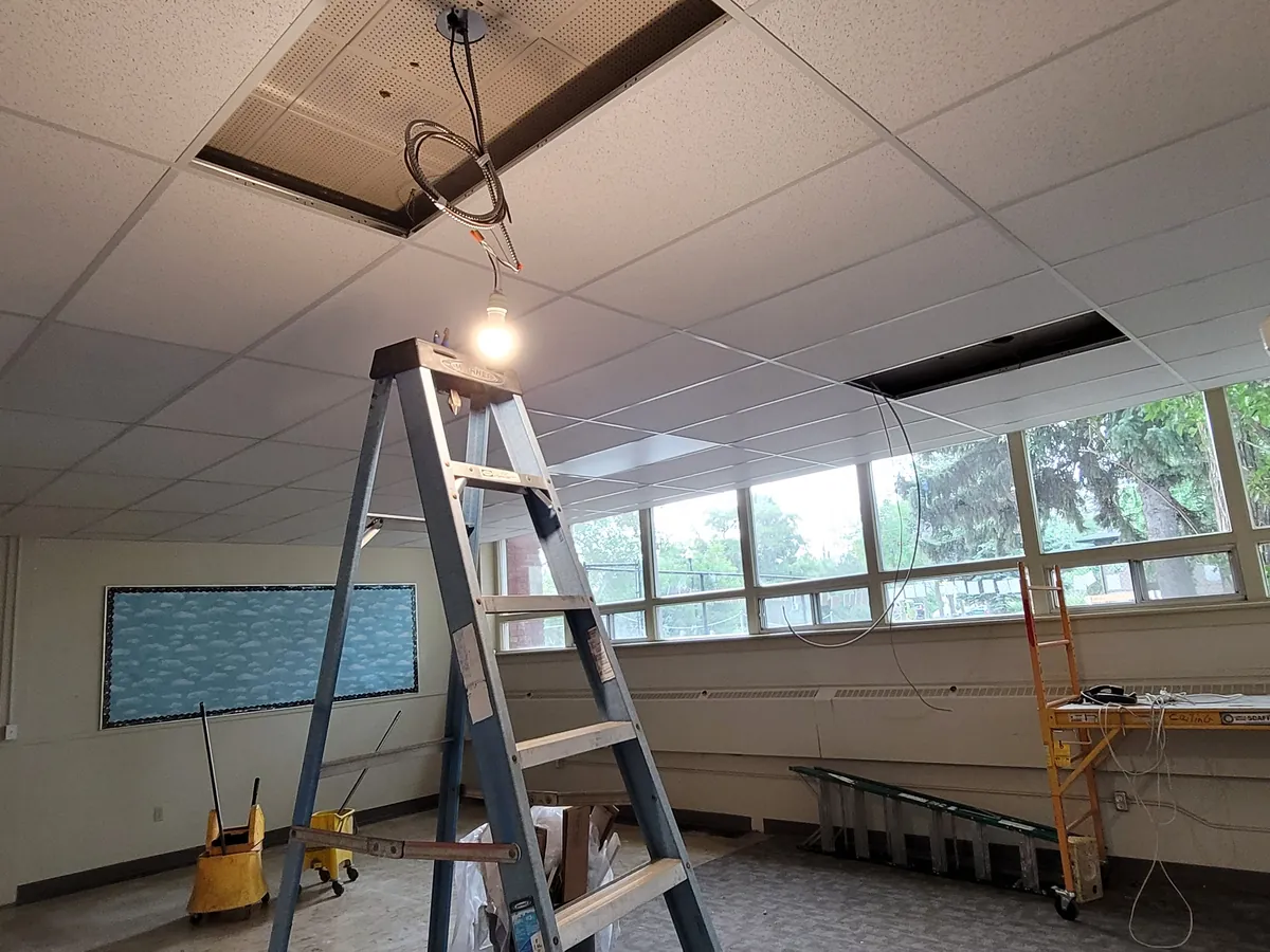 Before: a commercial room with ceiling tiles open and the old fixtures coming out