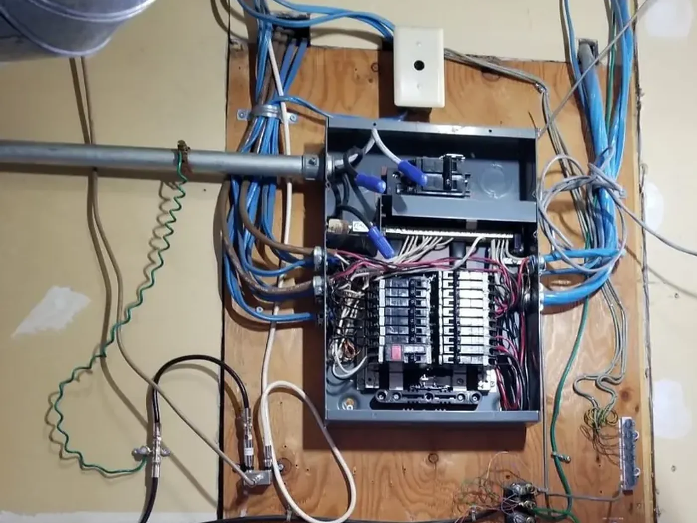 Before: open electrical panel with tangled circuit wiring on a plywood backer board, Edmonton basement