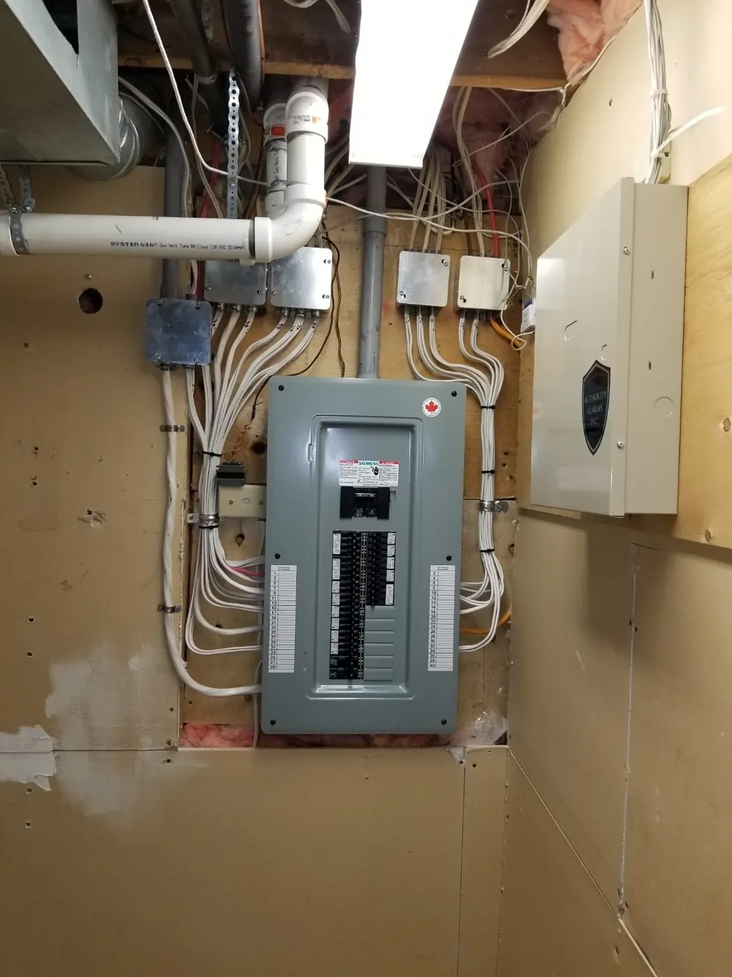 A new Siemens panel finished on an Edmonton basement wall with cables dressed into junction boxes above it and a printed circuit directory on the door