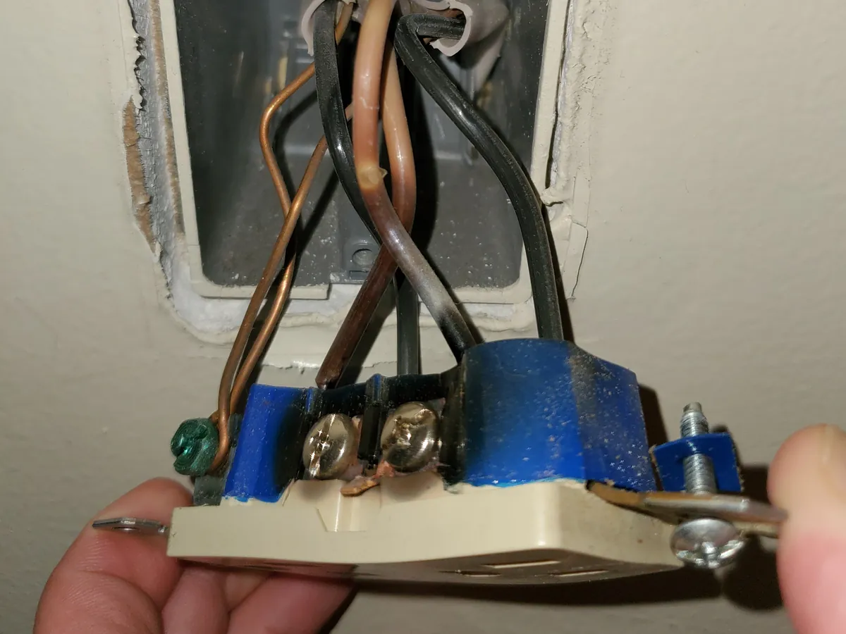 An old outlet pulled from the wall, its wires pushed into clips in the back instead of wrapped around the screws