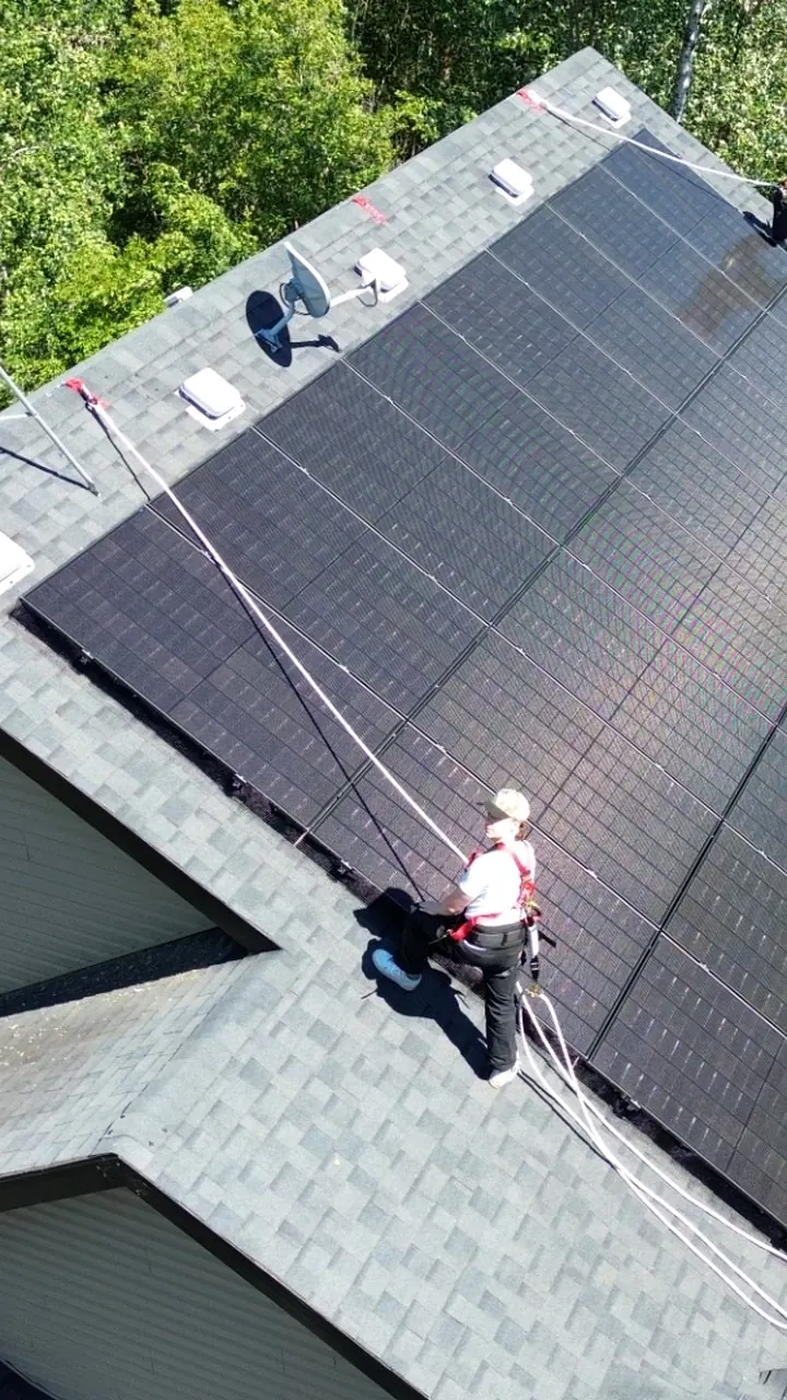 Raydn Renewables crew installing all-black solar panels on an Alberta lakefront roof, worker in safety harness mid-install