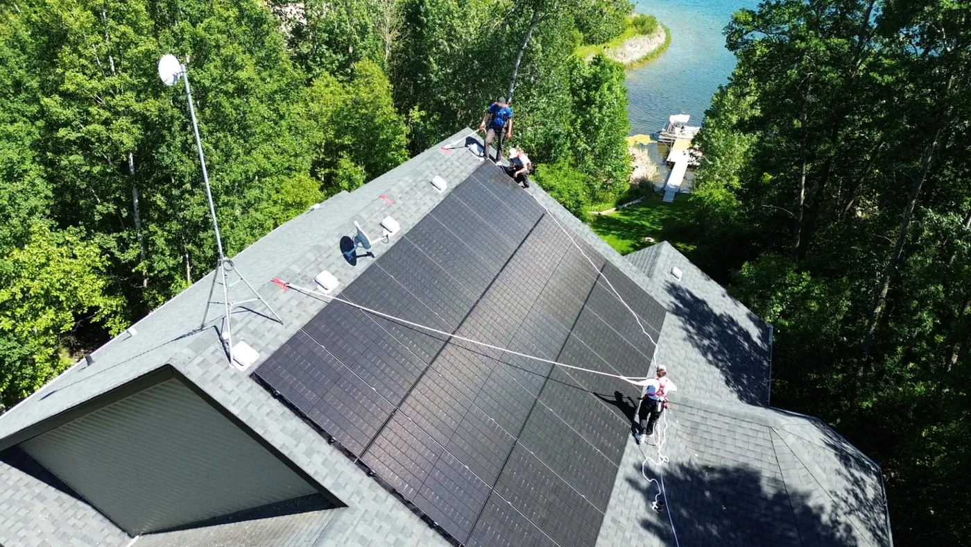Raydn crew installing all-black solar panels on a lakefront Alberta home, safety-harnessed, panels flush with the roof line.