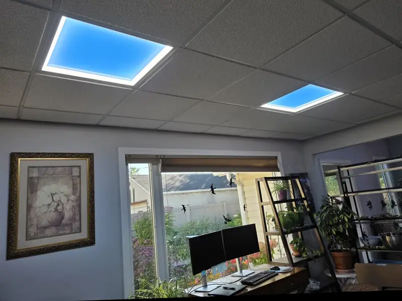 The same home office with two LED sky panels in the drop ceiling showing blue sky