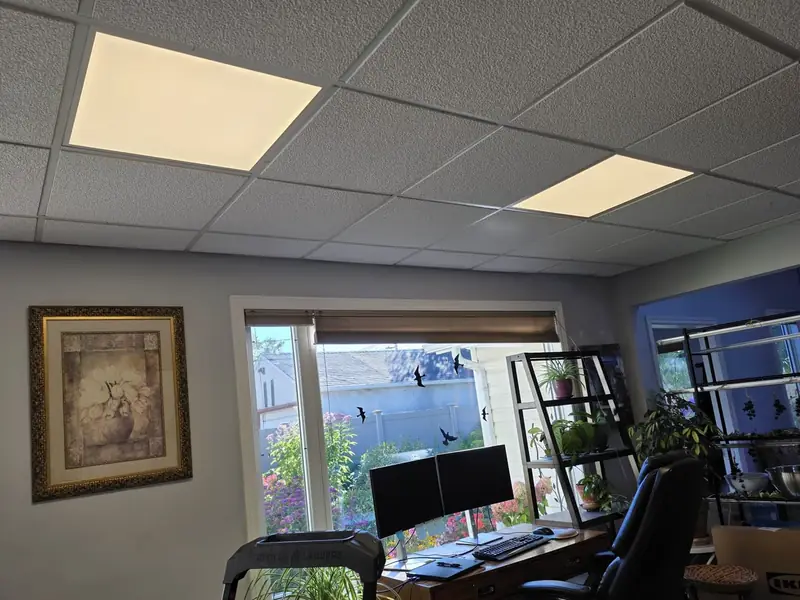 A home office in Edmonton before the work, lit by two flat 2 by 2 LED panels in a drop ceiling