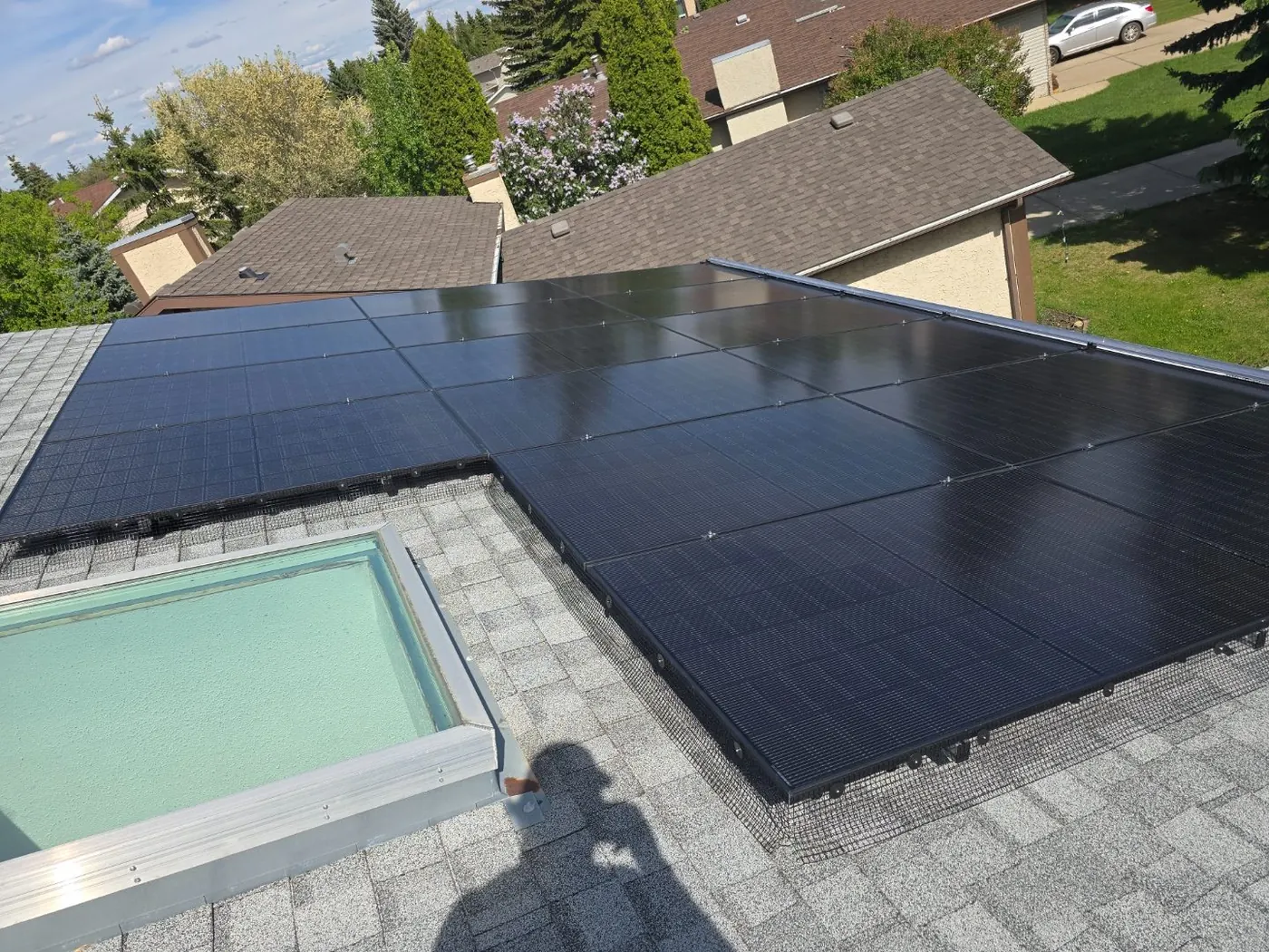 Black solar panels installed on light grey shingle roof around skylight, Edmonton suburb