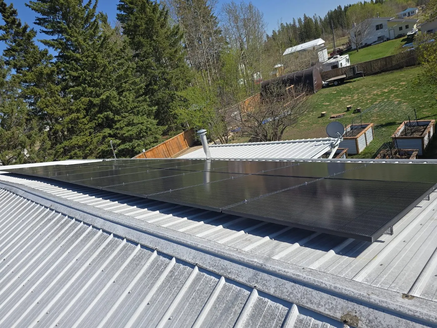 After: black solar panels fully installed on silver metal roof with rural treed backdrop Alberta