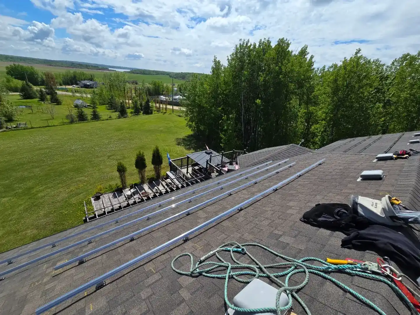 Before: dark charcoal shingle roof with solar mounting rails, rural river valley view Alberta