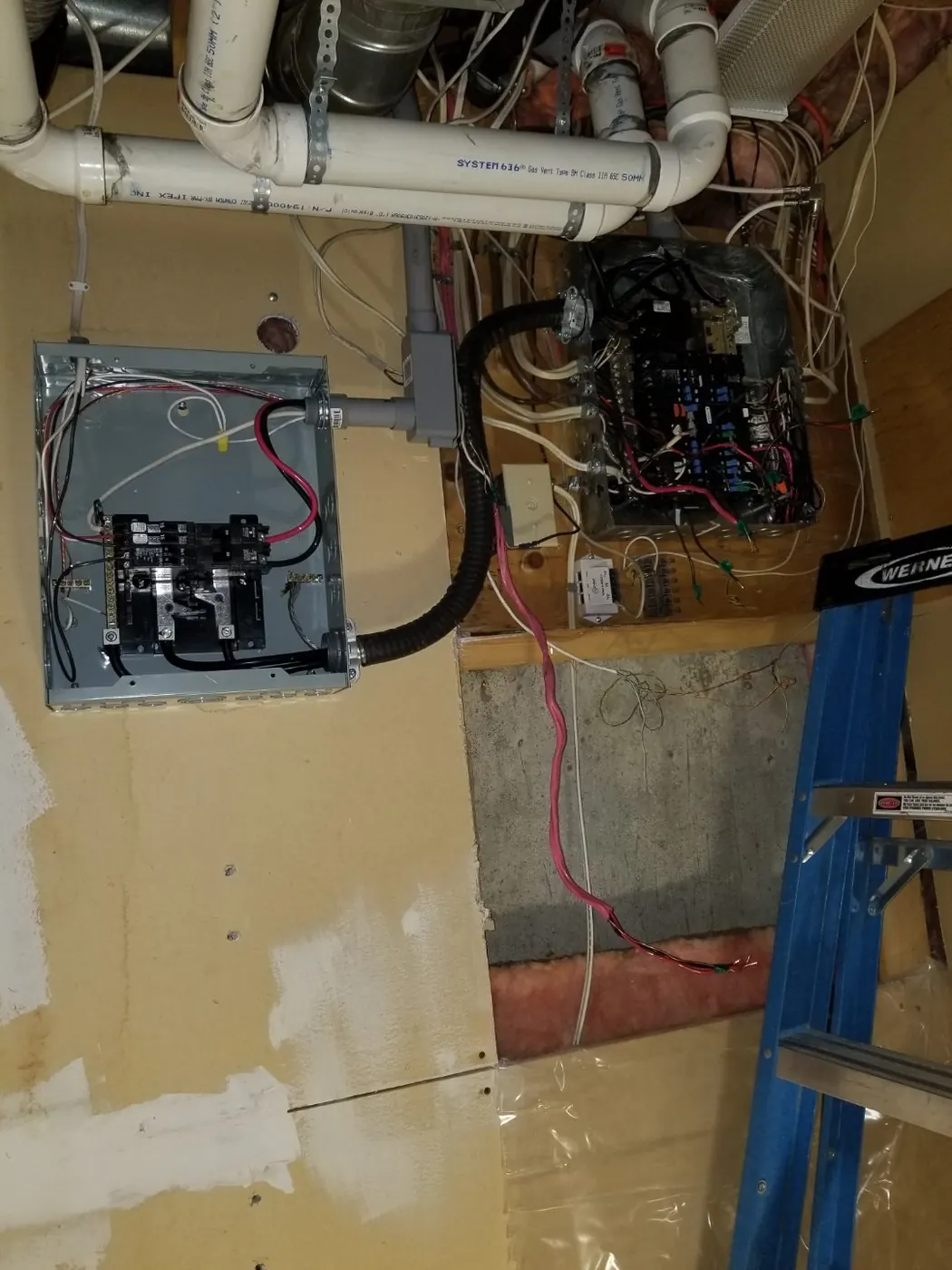 A new subpanel mounted beside an older crowded panel in an Edmonton basement, connected with flexible conduit, both covers off