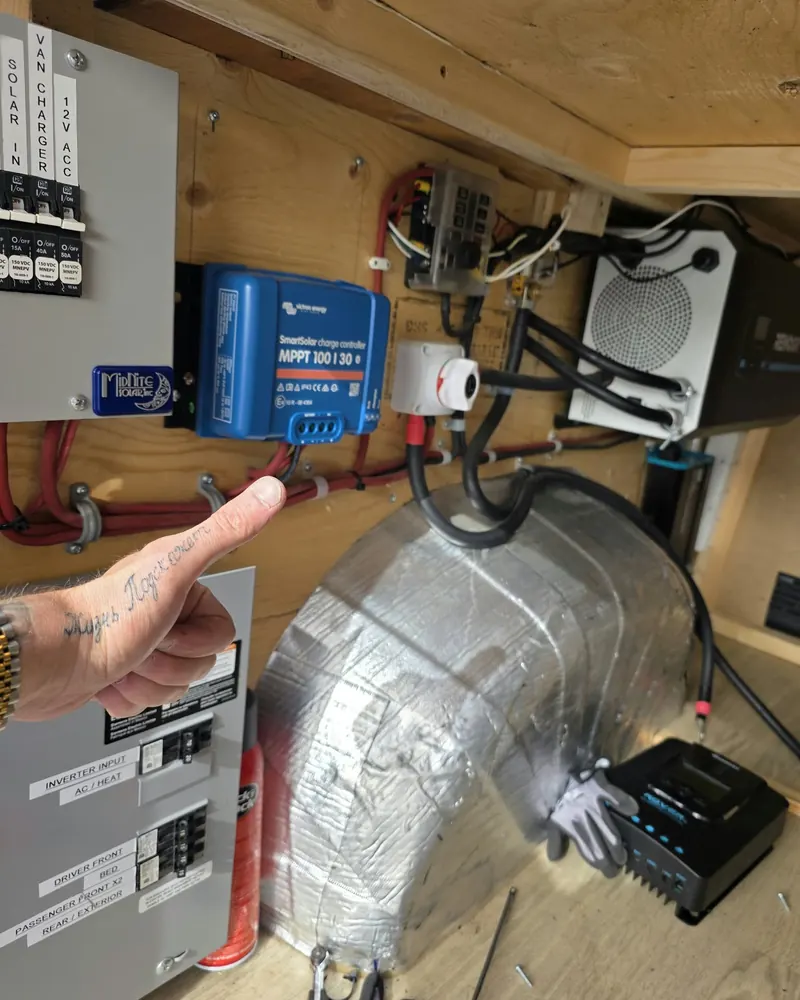 New blue solar charge controller on the van wall with a finger pointing at it, and the old black controller on the floor below